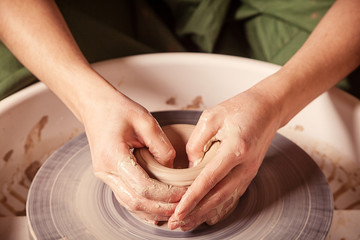 Close-up of a young woman potter beautifully sculpts a brown clay vase and makes for her neck on a potter's wheel, a top view