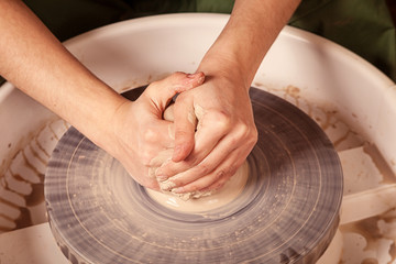 Close-up of a young woman sculpting a brown clay plate on a potter's wheel, top view