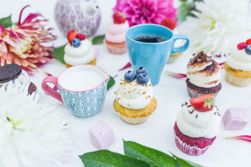 Cupcakes with fresh berries flowers and leaves, a cup of tea or coffee and a kettle.