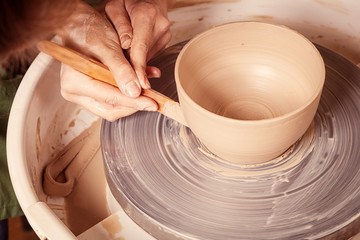 Close-up Woman potter beautifully sculpts from brown clay and equals a spatula with a deep plate on...