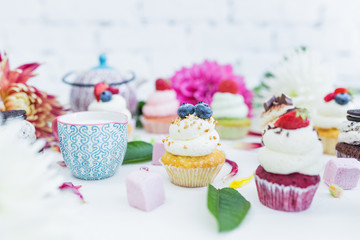 Cupcakes with fresh berries flowers and leaves, a cup of tea or coffee.