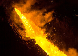 Tapping the blast furnace, liquid molten iron flowing out of the taphole of a blast furnace, lava-like. The iron temperature exceeds 1350 degrees Celsius.