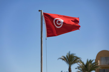 Tunisian flag waving in the blue sky in the beach