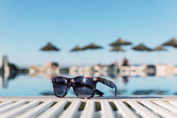 Fototapeta na wymiar Sunglasses by the pool, blue sky, swimming with sun umbrellas