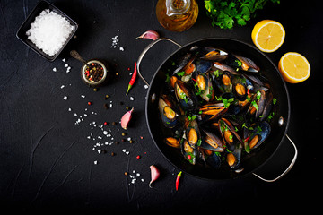 Mussels cooked in wine sauce with herbs in a frying pan on a black background. Flat lay. Top view.