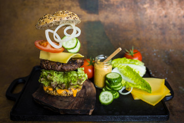 Hamburger with flying ingredients. Tasty smoked grilled and glazed beef burger with lettuce, cheese and vegetables on vintage background.