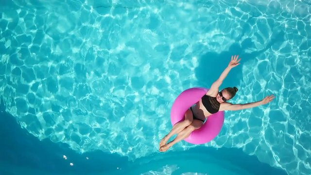 Top view fit girl enjoy pool in swimming circle and waved sunny drone footage