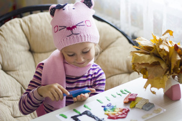 girl in hat and scarf sitting in the chair sculpts in the clay at the table