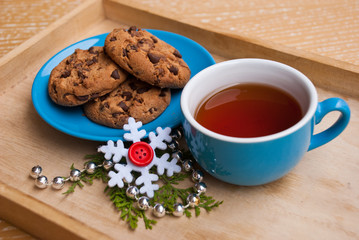 New year or christmas breakfast with cup of tea and plate with cookies chocolate on wooden tray. Decoration garland and snowflake.