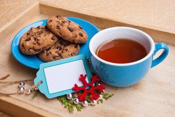 New year or christmas breakfast with cup of tea and plate with cookies chocolate on wooden tray. Decoration garland and snowflake and small label free.
