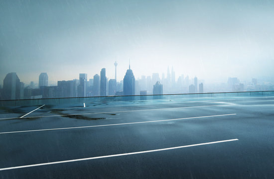 Empty Wet Asphalt Road With Foggy City Skyline Background , Raining Day .