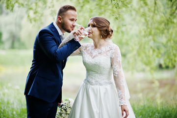 Newly married wedding couple drinking champagne in forest or park.