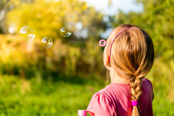 Beautiful young girl blowing soap bubbles in the summer park.