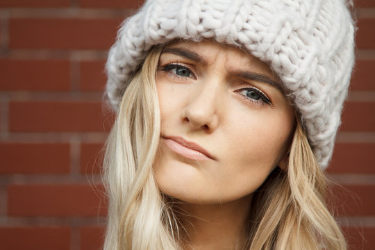 Portrait of a beautiful blonde woman wearing a large warm winter hat. Nice background of this composition is created of red brick wall.
