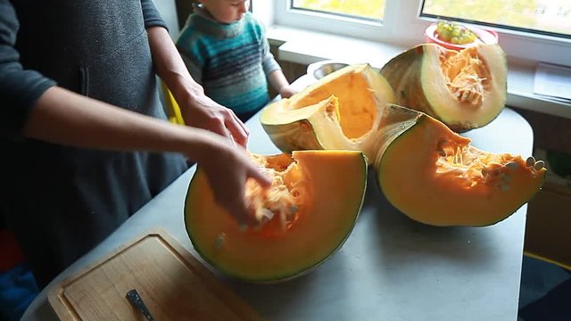 Video woman and a child are cleaning a big pumpkin on the kitchen table