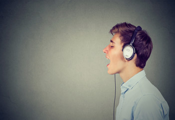 Handsome guy with headphones in blue shirt listening to music and singing