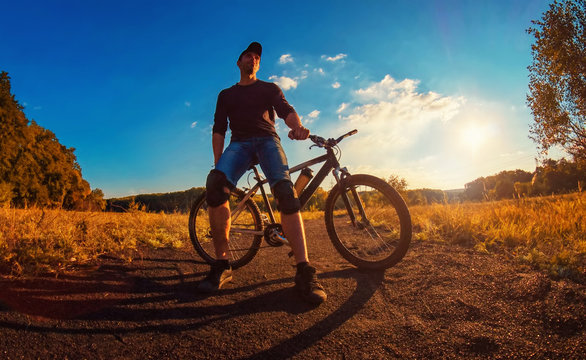 man in a black T-shirt,  blue jeans shorts and knee pads  relies on a sports bik