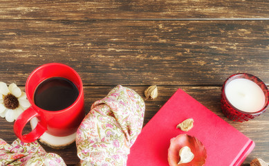 Red mug of herbal tea, floral silk scarf, red book and dry leaves on  the wooden background. Delicious cold weather beverage for fall times concept. Copy space