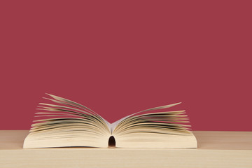 Open book with pages standing up lying on a bookplank on a red background