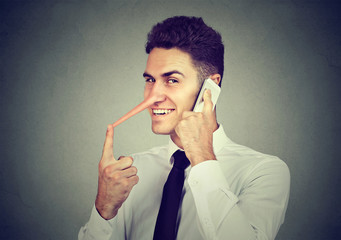 Sly young man with long nose talking on mobile phone isolated on gray wall background. Liar concept.