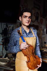 Obraz premium portrait of a young luthier with a handcrafted violin in his workshop with the tools.