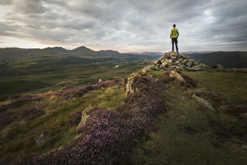 Strong hiker overlooking the beautiful mountains of the lake district at sunset with sunlight lit...