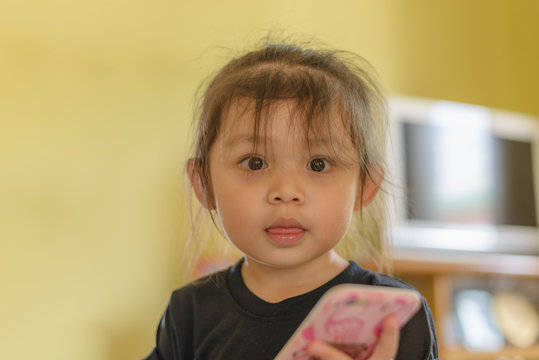 Cute Asian little girl hold smartphone in hand and looking straight on camera