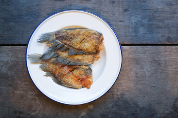 Crispy gourami fish in white plate on wood background