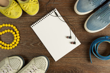 Women's shoes, yellow beads, blue belt, black headphones and white notebook flat lay