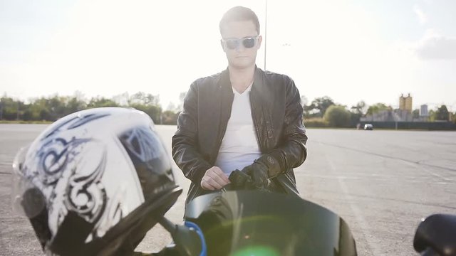 A motorcyclist who sits on a motorcycle in sunglasses and in a leather jacket, wears special leather mitts for riding