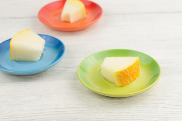 Three pieces of fresh yummy ripe melon on green and red and blue ceramic plate on old rustic white wooden background