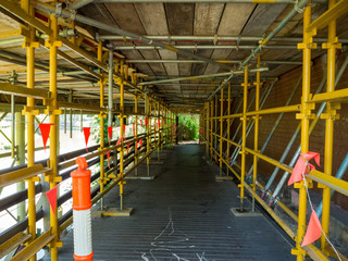 A footpath running through scaffolding underneath a bridge.
