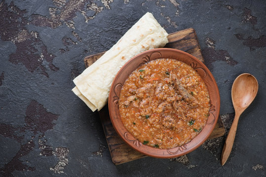 Georgian traditional kharcho soup served with lavash, flat-lay with space on a brown stone background