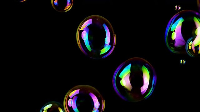 Colorful soap bubbles fly across black background.
