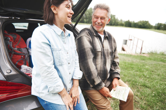 Mature couple in rural setting, standing beside car, laughing