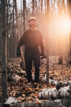 Male logger carrying chainsaw in sunlit autumn forest