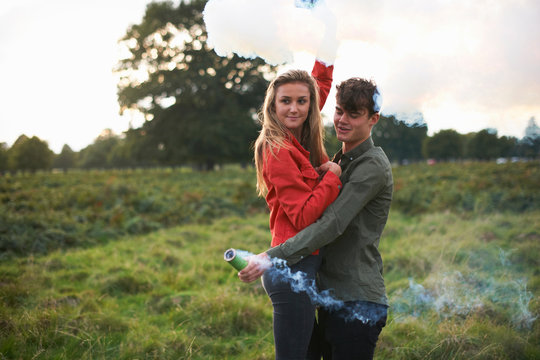 Young couple letting off smoke flares in field