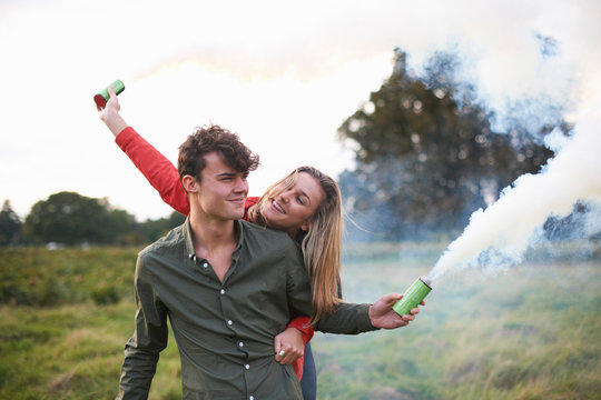 Young couple letting off smoke flares in field