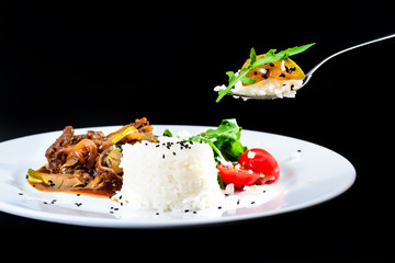 Process of eating dish. Delicious beef with oyster Mushrooms and rice served with tomatoes and sauce in a white plate over black background. Autumn menu in an Italian restaurant.