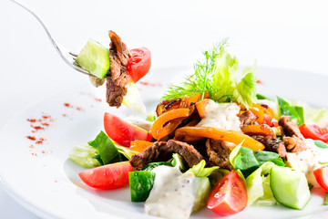 Process of eating roast beef salad with tomatoes, cucumbers, feta cheese and pepper. Dish in white plate over light background. Food background, menu design