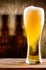 Fresh cold light beer in a glass with foam and drops of water on brown background