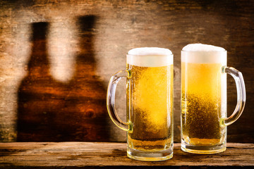 Two fresh cold light beer in a beer mug with foam and drops of water on brown background