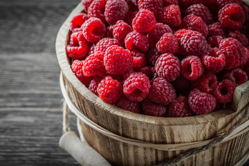 Raspberries in bucket on vintage wooden board close up view