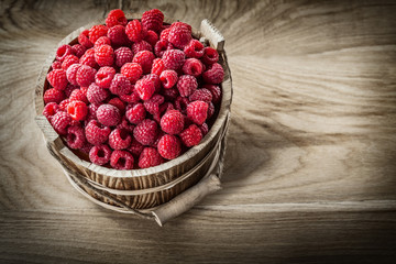Red raspberries in bucket on wooden board top view