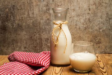 Un vaso de leche fresca y natural junto a una botella de cristal y un paño de cocina sobre un...
