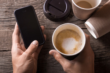 Man holds a phone in one hand and a cup of coffee in another. Excessive coffee harms your health