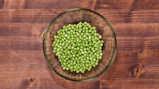 Peas slowly fill a glass bowl on the table - top view, timelapse