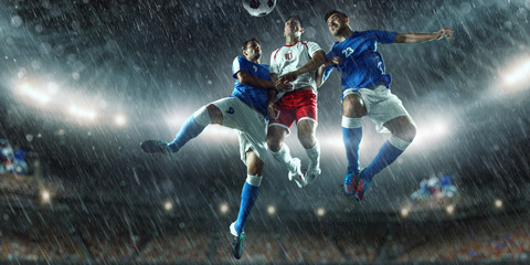 Soccer players performs an action play on a professional rainy stadium. Two football teams fighting...