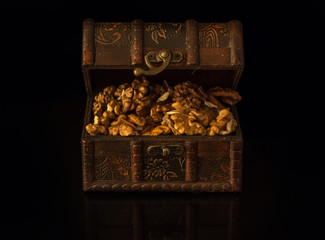 Broken walnuts in a retro styled old treasure chest, black background