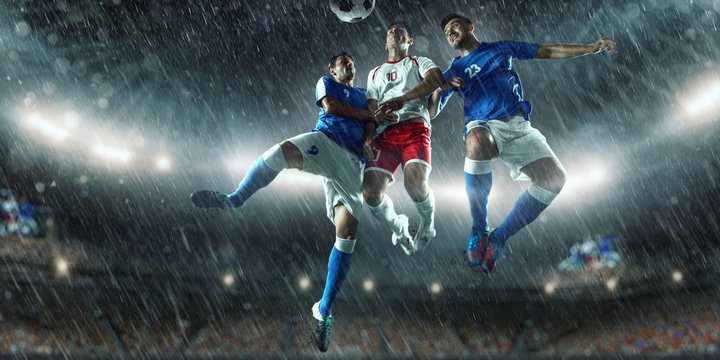 Soccer players performs an action play on a professional rainy stadium. Two football teams fighting for the ball. Players wears unbranded sport uniform.